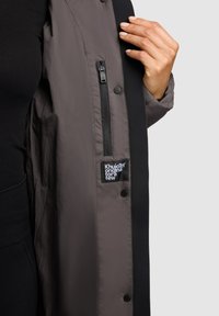 Gray, insulated jacket with a zippered pocket and a fabric label. The inner lining is smooth, while the external material has a matte finish.