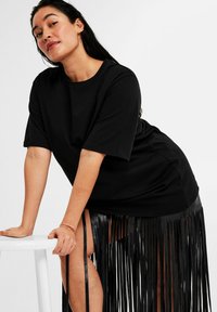 Mustat ylisuuret T-paidat lyhyillä hihoilla yhdistettyinä fringed-mustaan hameeseen, jossa on pitkiä, teksturoituja fringed-yksityiskohtia hemman reunalla.