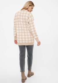 Beige Hahnentritt-Muster Pullover, runder Ausschnitt, lange Ärmel, weiche Stricktextur, kombiniert mit grauen Slim-Fit-Jeans und beigefarbenen Stiefeletten.