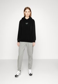 Svart hettegenser med logo på brystet, kombinert med lysegrå joggebukser og svart-hvite sneakers. Enkel, uformell stil.