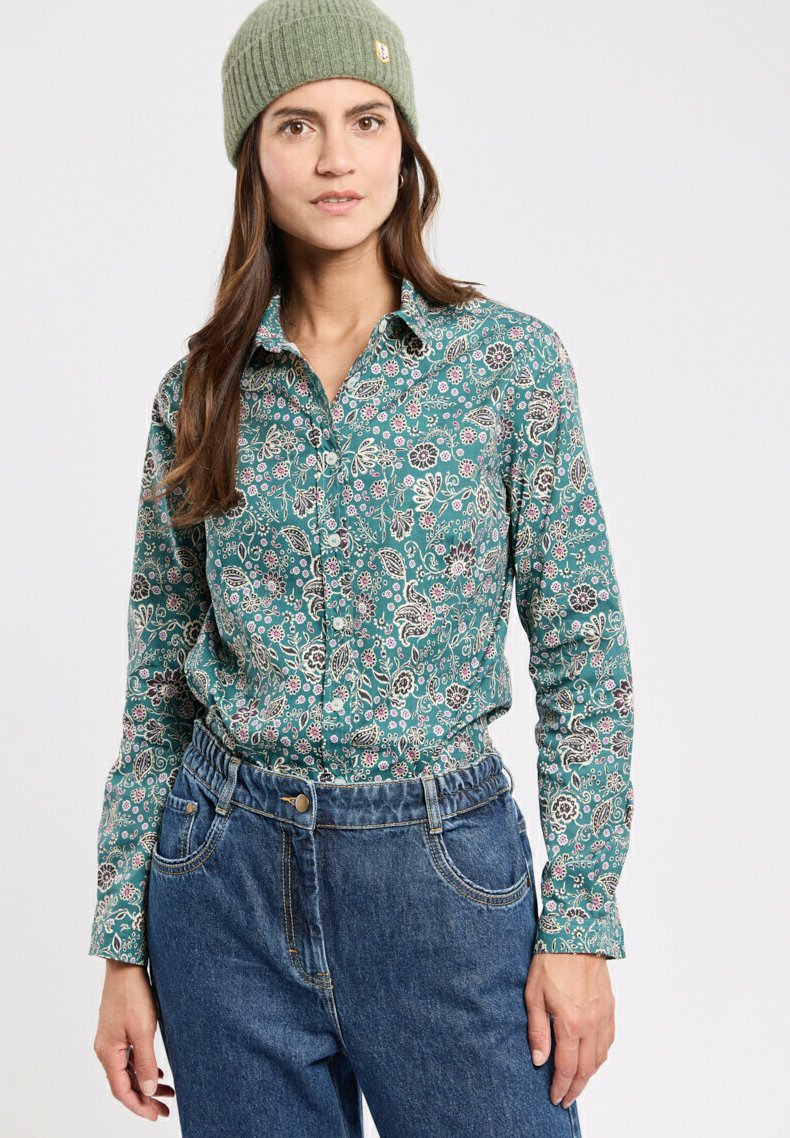 Türkisfarbendes, floral bedrucktes Hemd mit Knopfleiste und langen Ärmeln, kombiniert mit hoch taillierten blauen Jeans und einer hellgrünen Strickmütze.