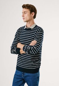 Jūras karaflotes un baltas svītras džemperis ar gaiši pelēku apkakli, ribotām piedurknēm un apakšmali. Valkāts kopā ar ziliem džinsiem, demonstrējot klasisku piegriezumu.