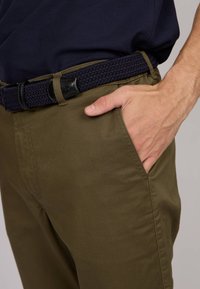 Pantalons vert olive avec une ceinture tressée navy texturée. Les caractéristiques incluent des poches avant et une finition en tissu lisse. Pas de motifs ou de logos visibles.