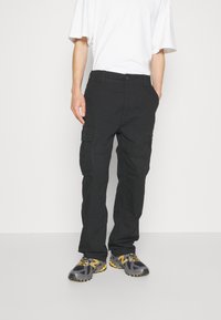 Svarta cargo byxor med flera sidofickor, en avslappnad passform och ett midjeband med knappstängning. Bärs med en vit t-shirt och sneakers.