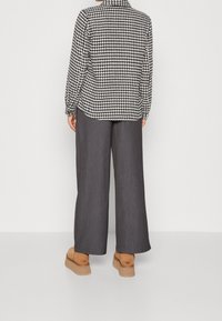 Camicia a maniche lunghe bianca e nera a motivo houndstooth, abbinata a pantaloni larghi grigio scuro e scarpe platform beige.