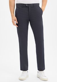 Donkergrijze stoffen broeken met een subtiel textuurpatroon, voorzien van een knoopsluiting, riemlussen en zijzakken, gecombineerd met witte sneakers.