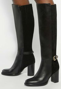 Black knee-high boots made of leather and suede, featuring a side zipper, strap with gold buckle accents, and square high heels.