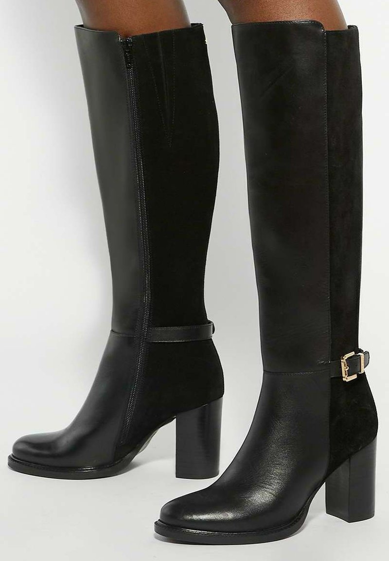 Black knee-high boots made of leather and suede, featuring a side zipper, strap with gold buckle accents, and square high heels.
