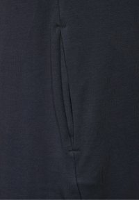 Musta laivastonsininen kangas, jossa on sileä pinta. Sisältää sivutaskun, jossa on huomaamaton sauman yksityiskohta. Yksinkertainen muotoilu ilman näkyviä kuvioita tai metalliosia.