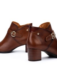 Botas de tobillo de cuero marrón con punta redondeada, un pequeño tacón cuadrado y una hebilla decorativa dorada en una correa. Textura suave con forro interior.