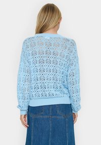 Jasnoniebieski sweter z dzianiny, cechujący się szczegółowym wzorem ażurowym, ściągaczami przy mankietach i u dołu, zestawiony z dżinsową spódnicą.