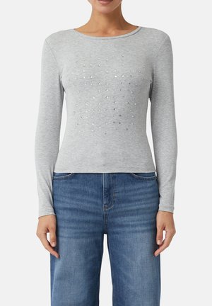 Helles graues Langarmshirt mit einem strukturierten, genoppten Design auf der Vorderseite, aus einem weichen Stoff gefertigt, kombiniert mit blauen Denim-Jeans.