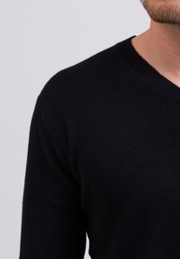 Maglione nero a V con un tessuto a maglia morbido e testurizzato, design aderente e maniche lunghe. Nessun motivo o dettaglio visibile.