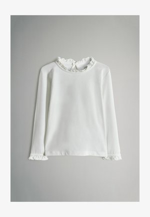 Bijela košulja dugih rukava s volanima oko ovratnika i manžeta, zatvaranje na gumbe na stražnjem dijelu ovratnika, položena ravno na sivoj podlozi.