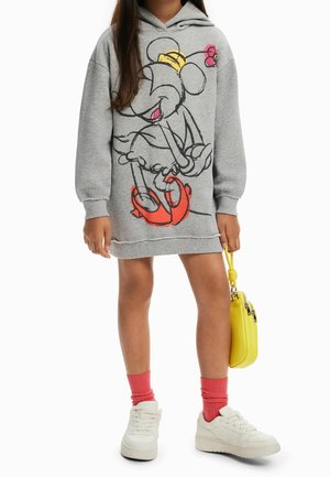 Niño con vestido con capucha gris con un gran dibujo de un ratón de dibujos animados, calcetines rosas, zapatillas blancas y sosteniendo un pequeño bolso amarillo.