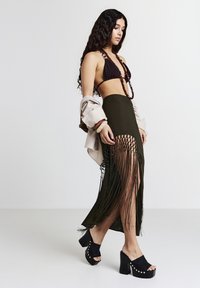 Gonna maxi verde oliva con frange e uno spacco alto, abbinata a un reggiseno triangolo marrone scuro e scarpe platform nere chunky.