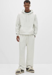 Grå hoodie med kengurulomme og snore, parret med matchende sweatpants. Materialet ser blødt og struktureret ud. Sneakers i mørke nuancer.