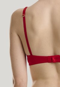 Rød bh med glat stof, smalle justerbare stropper og en hægtere lukning bagpå. Tekstureret kant på stropperne.