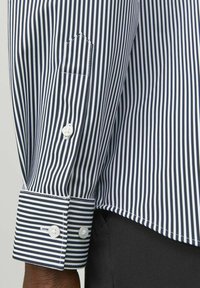 Camicia a righe navy e bianca con polsini abbottonati, tessuto interno a contrasto e una piccola tasca sul petto con patta appuntita.