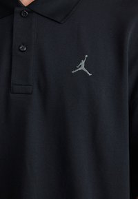 Čierne polo tričko s dvoma gombíkmi, textúrovanou tkaninou a šedým vyšívaným logom Jumpman na ľavej strane hrudníka.