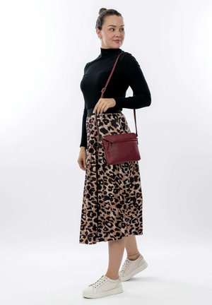 Haut noir à manches longues côtelé, jupe plissée beige à imprimé léopard, et baskets blanches. Sac à bandoulière bordeaux assorti avec détail zippé.
