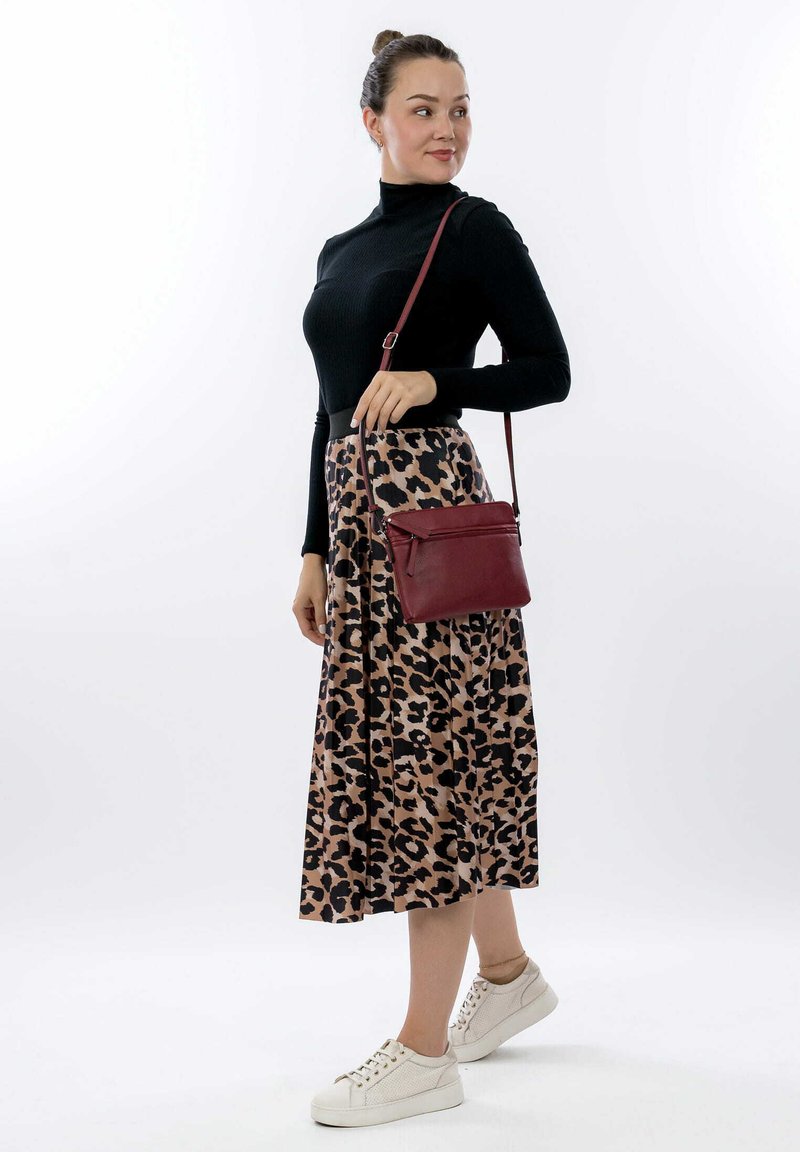 Top de manga larga negro con relieve, falda plisada de leopardo beige y zapatillas blancas. Bolso cruzado burdeos a juego con detalle de cremallera.
