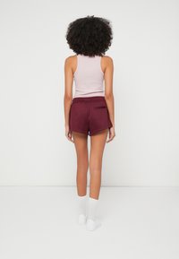 Μπορντό αθλητικό σορτς με άνετη εφαρμογή, πλαϊνές τσέπες και ελαστική μέση, συνδυασμένο με ανοιχτό ροζ τοπ και λευκές κάλτσες.