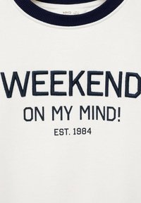 Felpa bianca con colletto a costine blu navy. Presenta un testo ricamato: "WEEKEND ON MY MIND!" e "EST. 1984" in blu scuro. Design orientato al comfort.