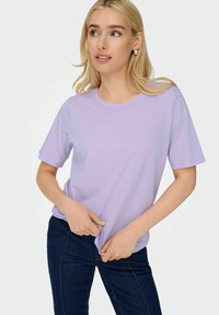 Lys lavendel kortærmet t-shirt i blødt stof med rund halsudskæring. Kombineret med mørkeblå jeans, der fremhæver det afslappede tøjdesign.