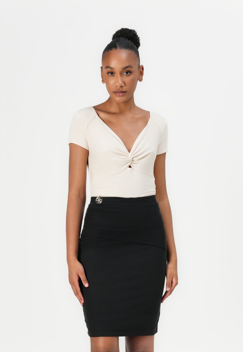 Beige aansluitend top met een gedraaide voorkant, korte mouwen. Zwarte penceletui met een gestructureerde afwerking en zilveren accent in de taille.