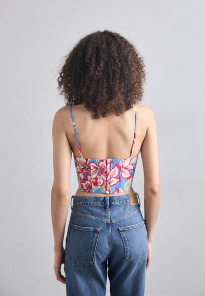 Blomster mønstrete crop topp med blå bakgrunn, tynne stropper og en strukturert design, kombinert med høyt skjørtet blå denimbukser.