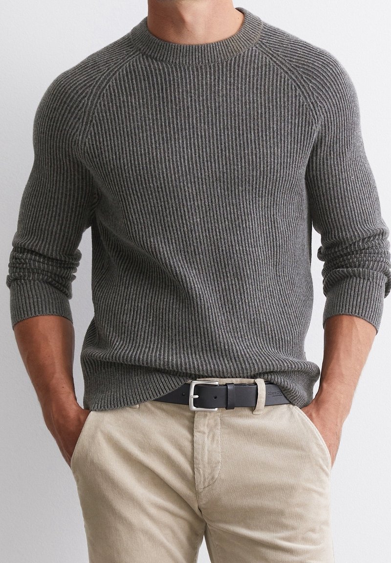 Šedý žebrovaný svetr s kulatým výstřihem, s dlouhými rukávy a texturovaným vzorem. Kombinován s lehce béžovými manšestrovými kalhotami a černým pásem.