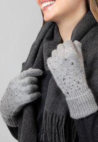 Grijze gebreide handschoenen met decoratieve kralen, geribbelde manchetten, gedragen met een donkergrijze sjaal. Focus op de textuur en details van de handschoenen.