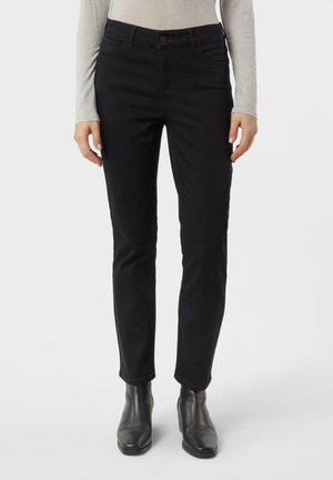 Jeans neri slim-fit indossati con stivaletti neri fino alla caviglia e una maglietta grigia chiara a maniche lunghe, mostrati dalla vita ai piedi su sfondo bianco.