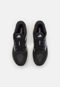Chaussures de sport noires avec un dessus en maille respirante, un design à trois rayures blanches, un motif texturé et une semelle rembourrée.