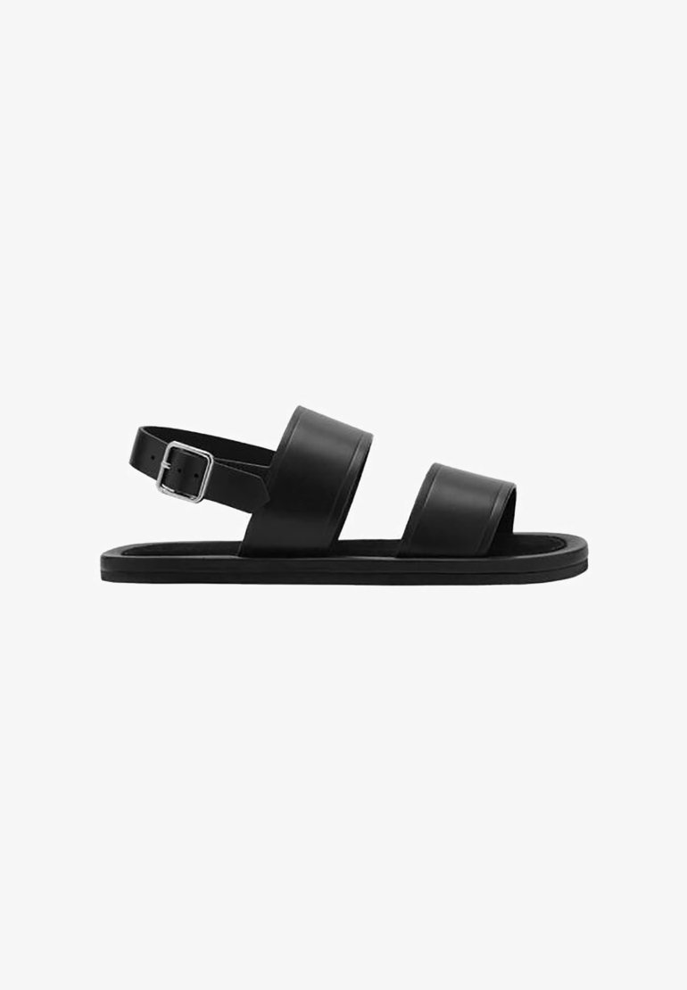 Sandalias negras hechas de material suave, con dos correas anchas y una correa en el talón con hebilla, con suela plana y diseño minimalista.