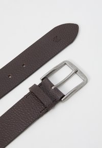 Ceinture en cuir marron texturé avec une boucle rectangulaire en métal argenté et des trous de perforation pour l'ajustabilité. Logo de la marque embossé sur la sangle.