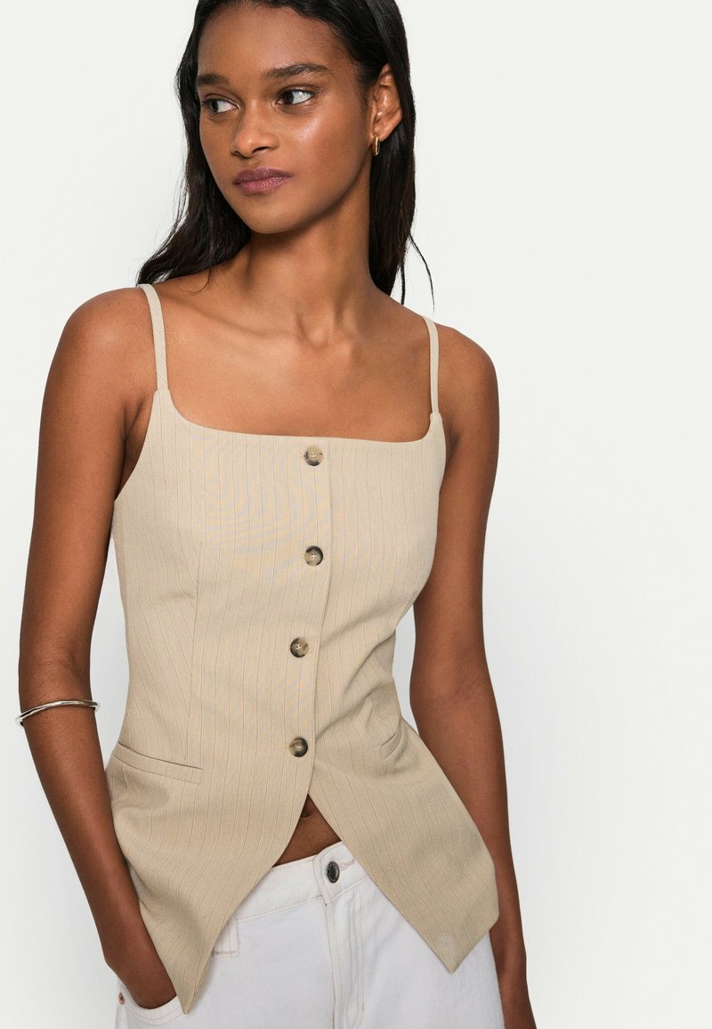 Beige, randig camisole med fyrkantig halsringning, med framknappar och en åtsittande design. Inkluderar sidofickor och en delad fåll.