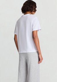 T-shirt bianca a maniche corte con taglio dritto e scollo rotondo, abbinata a pantaloni grigi a gamba larga. Tessuto dalla texture liscia.