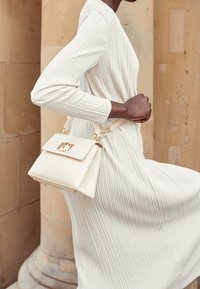 Kremowa torba na ramię o strukturalnym, kwadratowym kształcie. Posiada zapięcie na klapę, złote akcenty oraz odczepiany pasek na ramię. Teksturowane wykończenie.