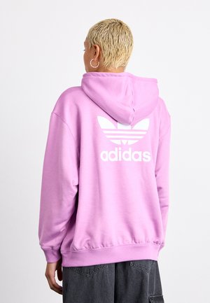 Vaaleanpunainen huppari, jossa on valkoinen Adidas-logo ja kolme raitaa selässä. Pehmeä kangas, jossa on ribbikangas hihansuissa ja helmassa.