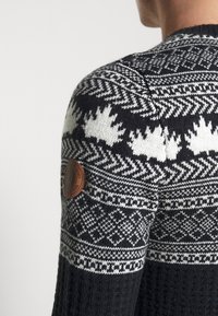 Gebreide trui in zwart en wit met trui ontwerp, gekenmerkt door een gestructureerd patroon en een bruine leren patch op de bovenarm.