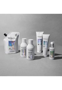Sept produits de soin capillaire Redken Acidic Bonding Concentrate disposés sur une surface grise avec différentes formes et tailles de bouteilles.