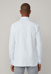 White long-sleeve shirt with a classic collar, featuring button cuffs and a smooth texture. Back view showcases a clean, minimalist design.