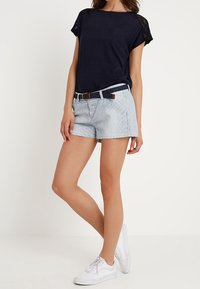 Top navy con detalles de encaje, pantalones cortos ligeros a rayas y un cinturón trenzado. Zapatillas blancas completan el conjunto. Diseño minimalista y ajuste casual.