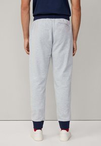 Grijze sweatpants van zachte stof, met een taps toelopende pasvorm, marineblauwe boorden en een achterzak, gecombineerd met witte sneakers en rode sokken.