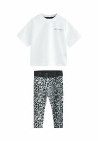 Bijela pamučna majica s "ALLSAINTS" logom na prsima; uparena s crnim i sivim tajicama s printom leoparda koje imaju široki crni pojas.