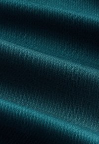 Tmavá tyrkysová látka s jemným cikcak textúrovaným vzorom a mäkkými záhybmi vytvárajúcimi kontrasty tieňa a svetla.