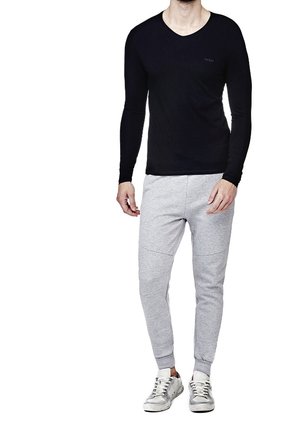 Maglietta nera a maniche lunghe con scollatura a V abbinata a pantaloni della tuta grigi chiari con cuciture laterali, polsini a coste e sneakers bianche sportive.