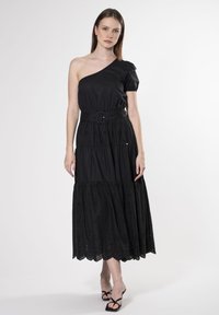 Vestido negro de un solo hombro con manga abullonada, diseño en capas y cinturón en la cintura. Presenta detalles bordados y un dobladillo con forma de concha.
